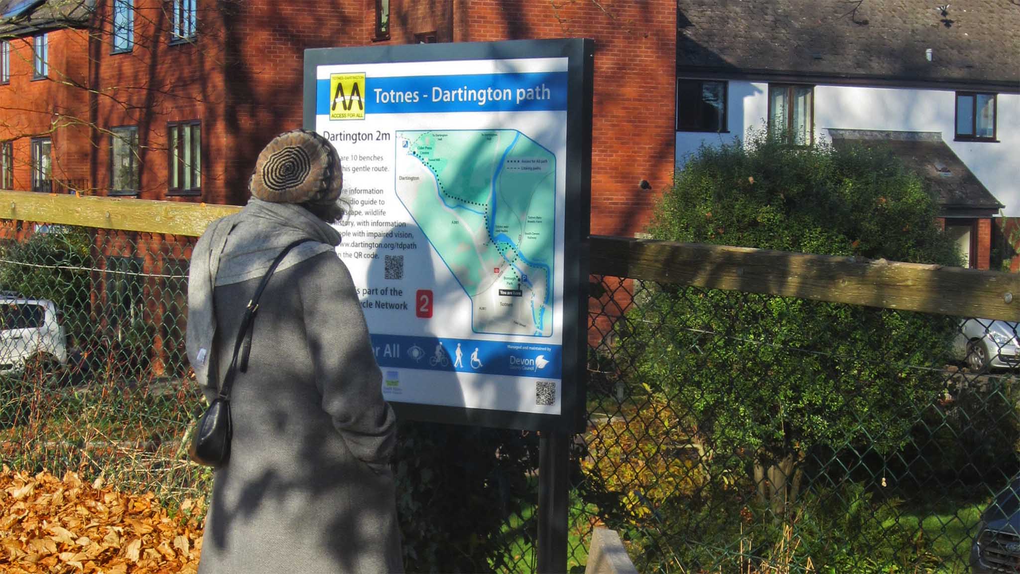 A woman wearing a grey coat looks at the new information board in Borough Park